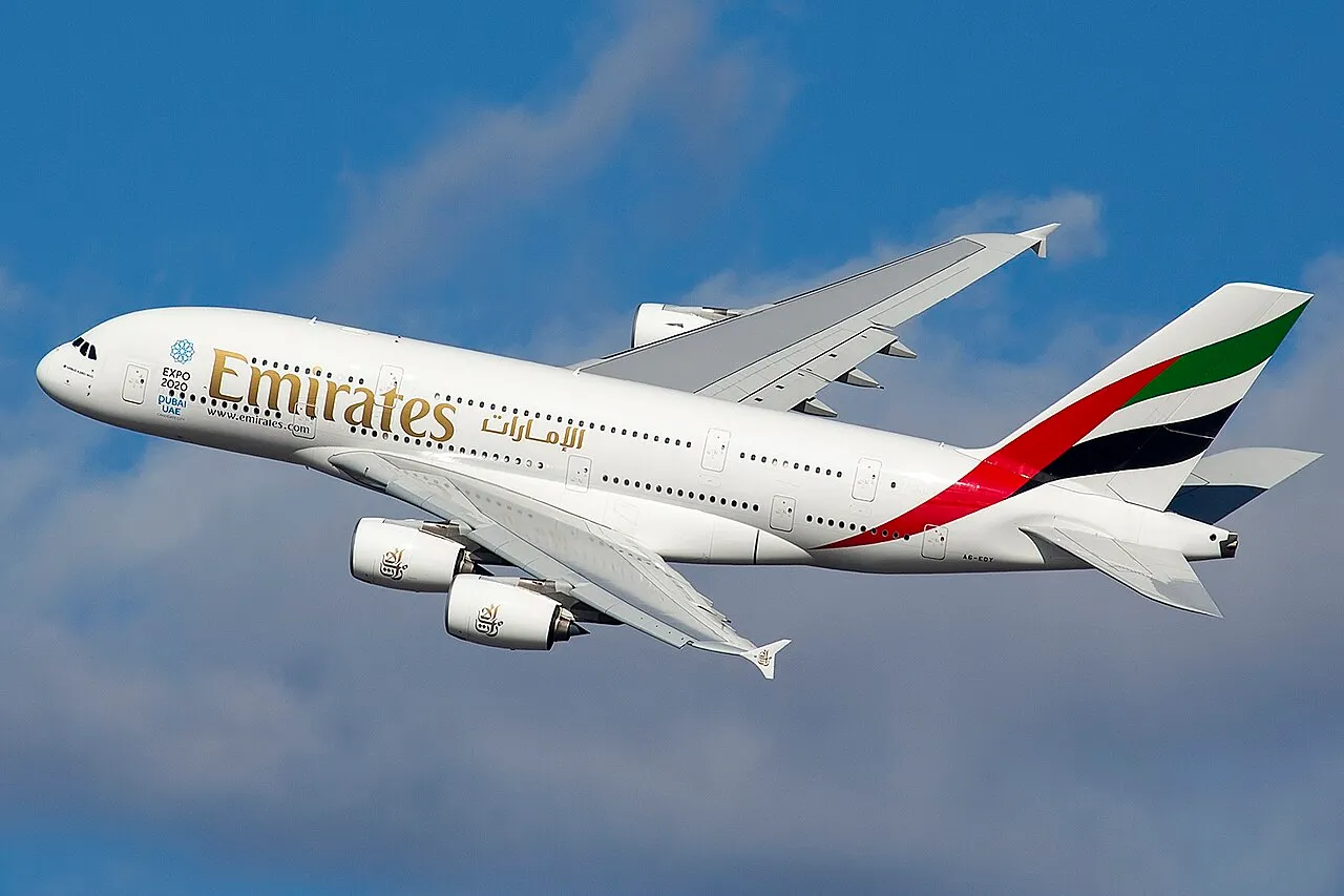 An Emirates Airbus A380 climbing against a blue sky, its four engines and double row of cabin windows in view.
