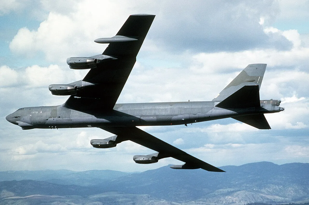 An air-to-air view from below a camouflaged B-52G Stratofortress bomber in flight.