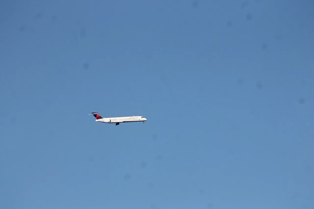 A Delta Air Lines Boeing 717-200 in flight over the Pacific Ocean, heading toward an airport.