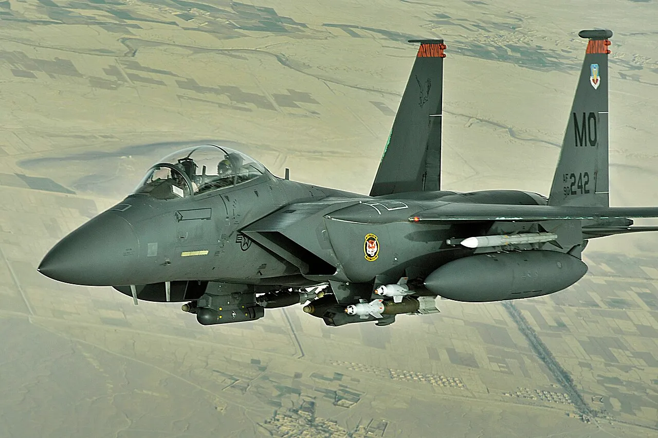 An F-15E Strike Eagle in flight over Afghanistan, viewed from below against a hazy sky.