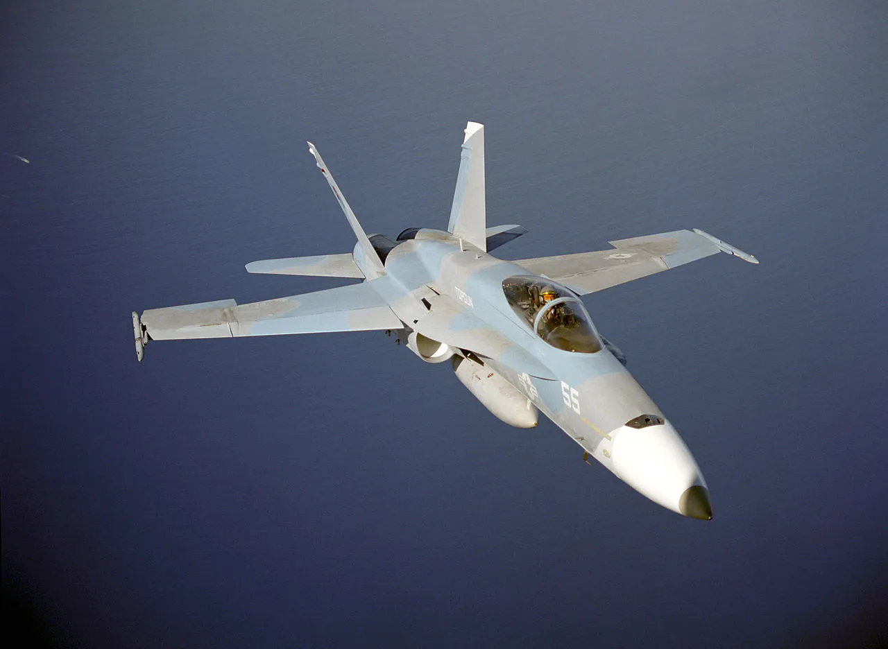 An F/A-18 Hornet from the US Navy TOPGUN school flying low over open water.