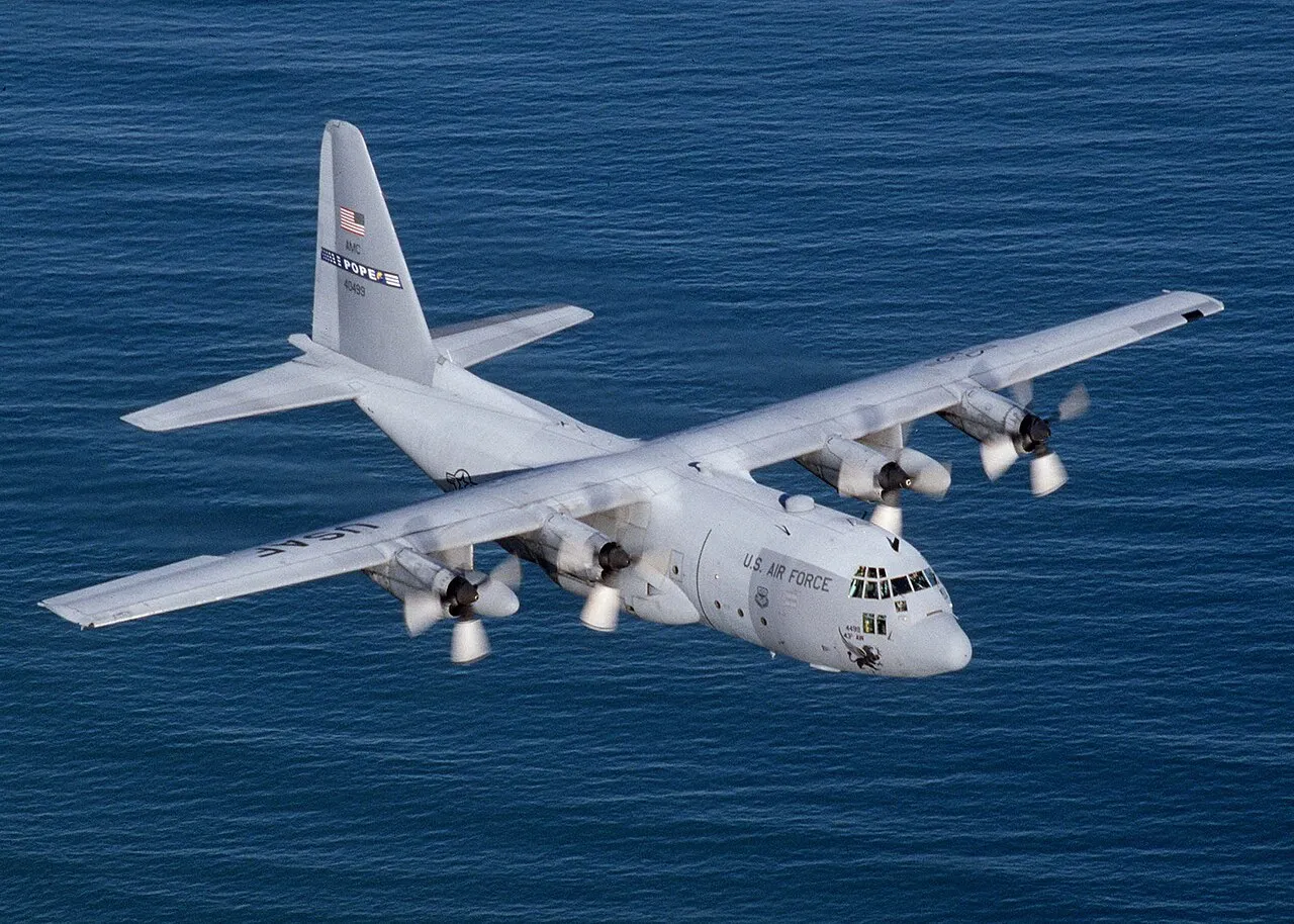 A U.S. Air Force C-130E Hercules transport plane flying over the Atlantic Ocean, its four turboprop engines visible on the straight wing.
