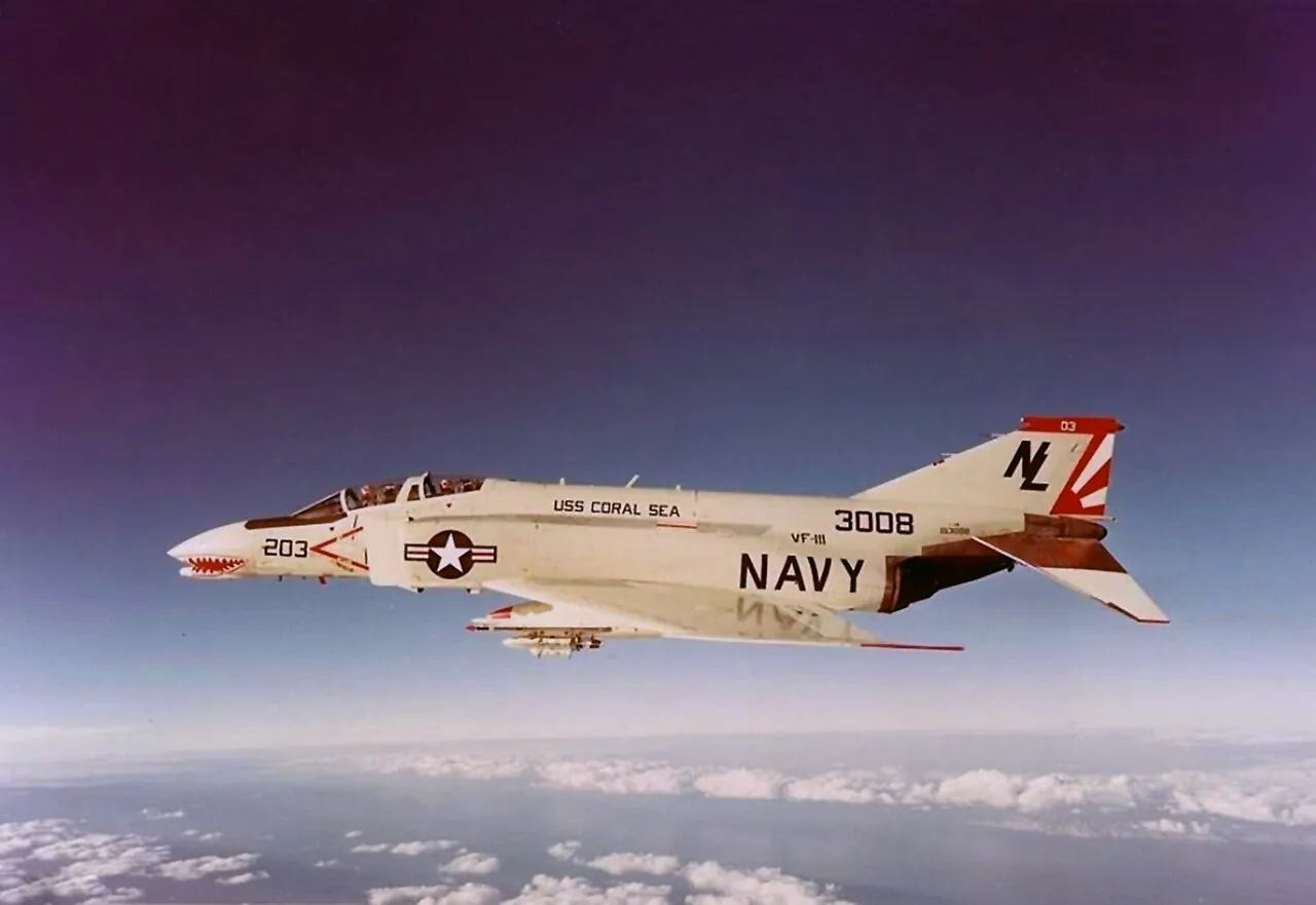 A grey U.S. Navy McDonnell F-4B Phantom II fighter jet banking in flight above clouds.