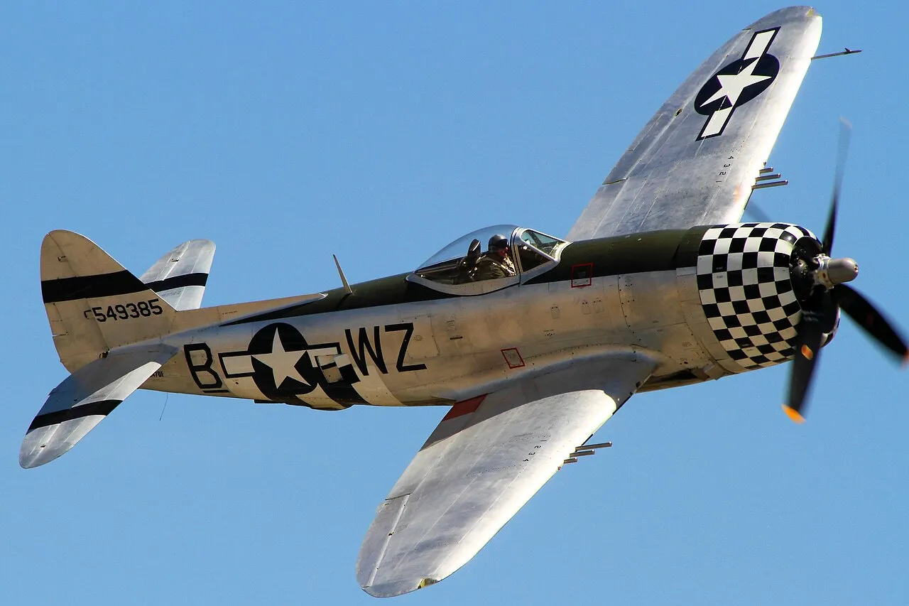 A restored silver P-47 Thunderbolt fighter on display at the Chino Airshow, showing its barrel-shaped fuselage and bubble canopy.