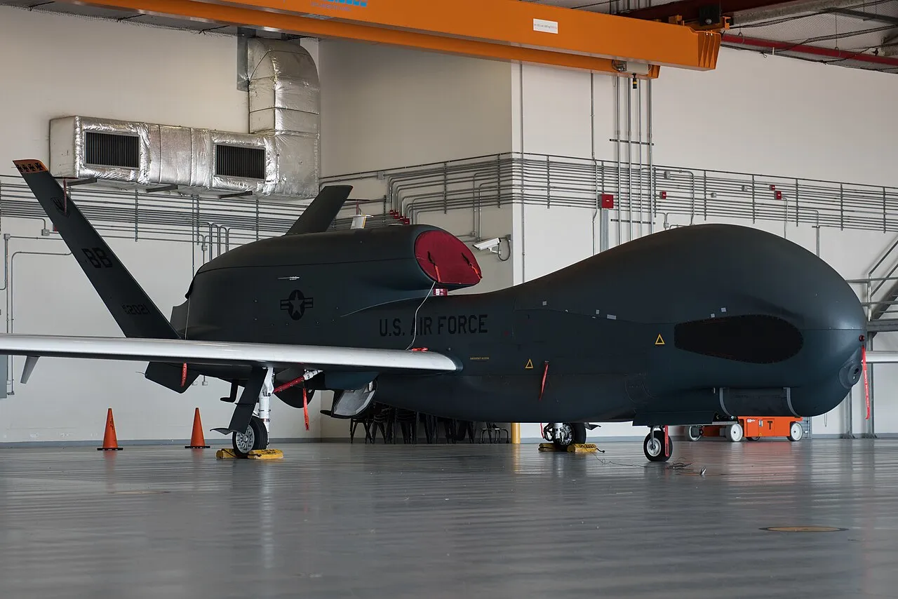 An RQ-4 Global Hawk sits static in a hangar at Naval Air Station Sigonella, Italy, showing its long, straight wings and bulbous nose radome.