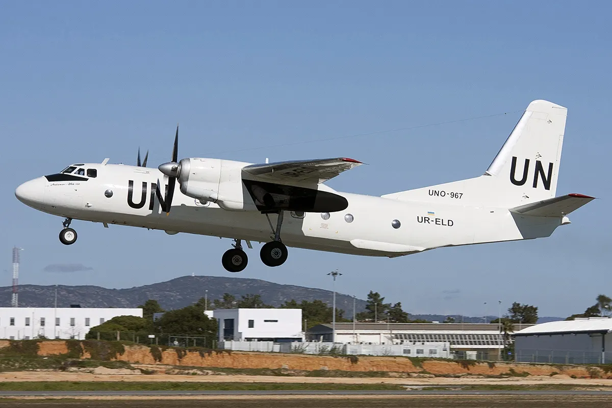 An Antonov An-26B twin-turboprop transport aircraft of Air-Urga on the ground, its high wing and rear cargo ramp visible.