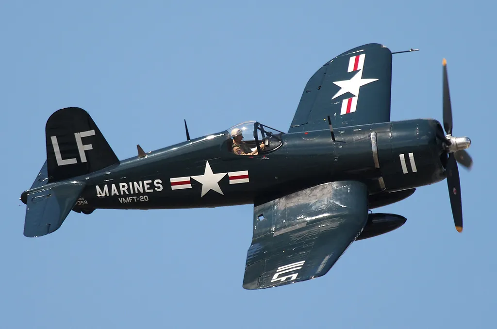 A Vought F4U Corsair in U.S. Marine Corps markings, in flight against a clear sky, showing its distinctive inverted gull wings.
